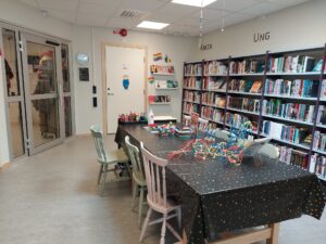 Foto på mellanrummet på Vaggeryds bibliotek med ett stort bord i mitten och lila bokhyllor mot väggen.