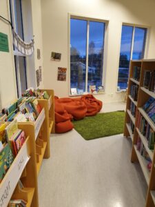 Bilderbokstråg till vänster, en bokhylla till höger och en grön matta och röda puffar på golvet rakt fram