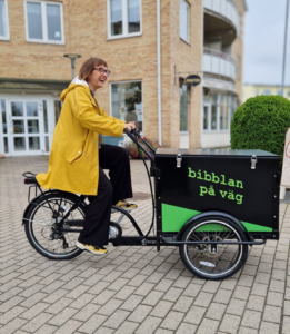 Kvinna i gul regnjacka på en lådcykel som det står Bibblan på väg.